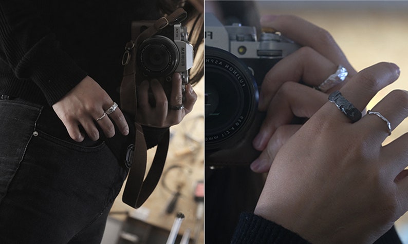 May include: Close-up of hands wearing various silver rings. The rings have different textures and designs, including a textured band, a hammered metal ring, and a delicate, wavy ring. The person is holding a camera.