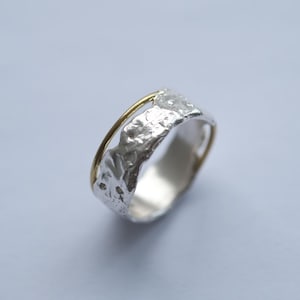 Puede incluir: Un anillo de plata con una banda texturizada y una fina banda dorada envuelta alrededor.