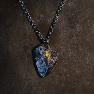 Könnte beinhalten: Eine silberne Kettenkette mit einem Anhänger in Form eines zerklüfteten Steins. Der Anhänger ist aus Silber und hat ein kleines Stück Blattgold darauf.