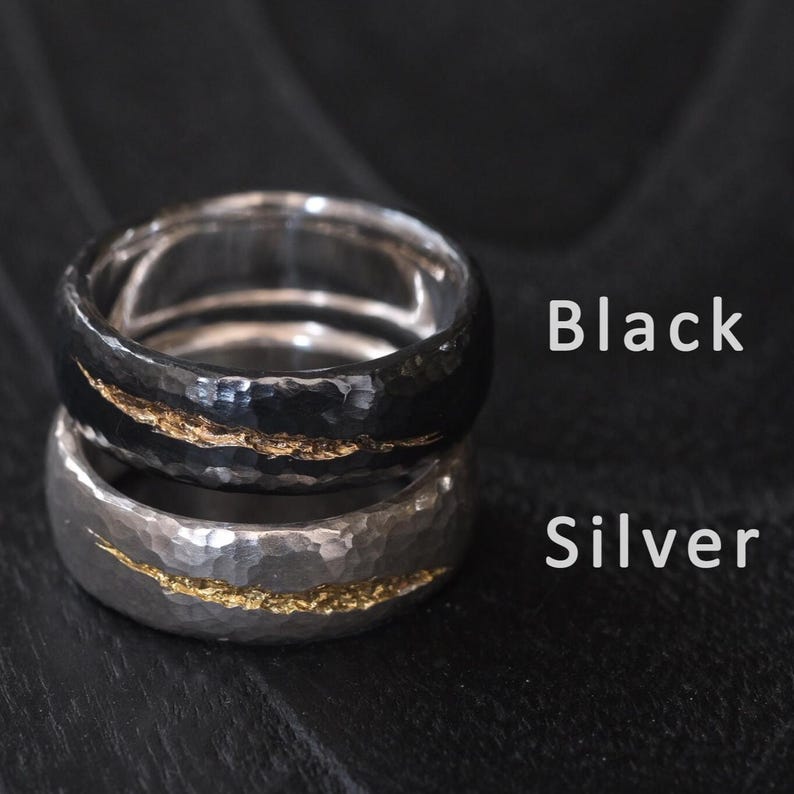 Puede incluir: Dos anillos de metal martillados con una fina franja dorada. El anillo superior es negro y el anillo inferior es plateado. Los anillos est&aacute;n etiquetados como "Negro" y "Plata".