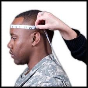 May include: A person's head is measured with a white measuring tape. The tape is wrapped around the head, showing the measurement in inches. The person is wearing a camouflage shirt.