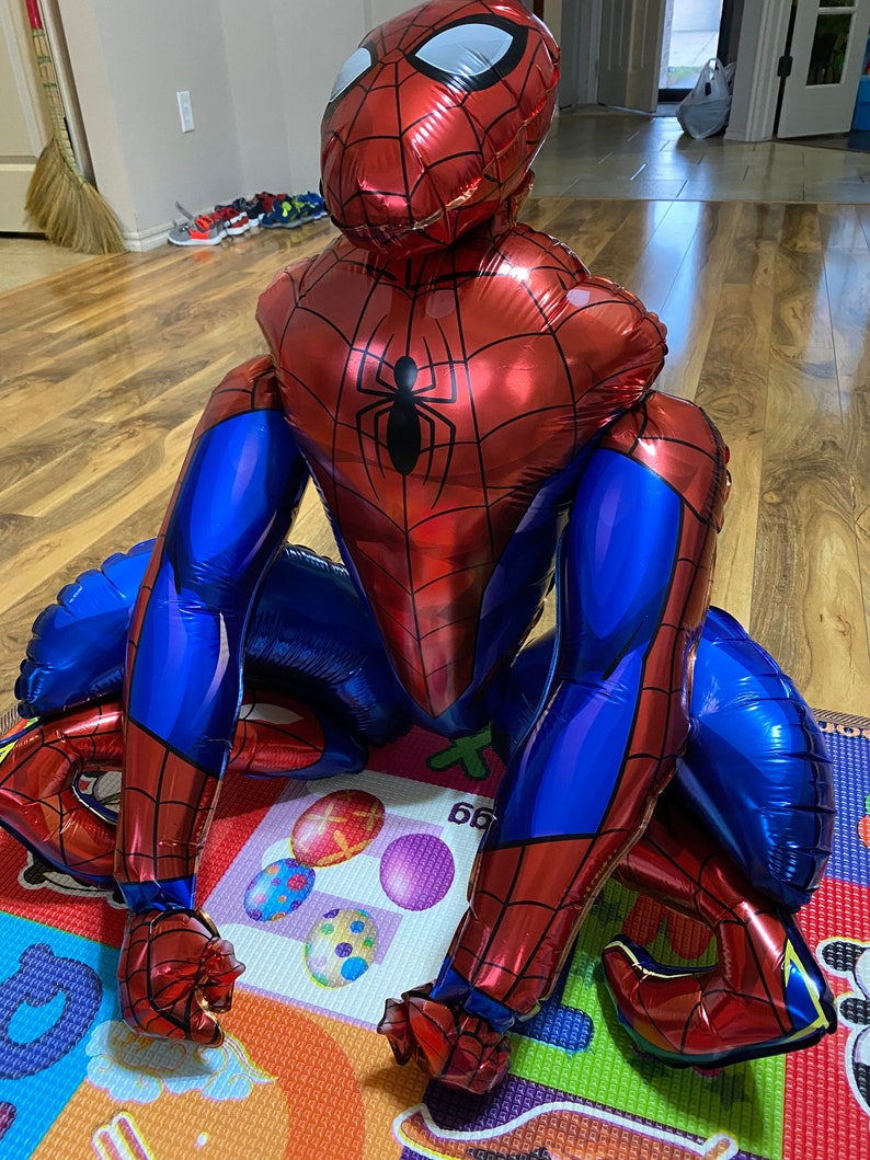 K&ouml;nnte beinhalten: Ein gro&szlig;er roter und blauer aufblasbarer Spiderman-Ballon mit einem wei&szlig;en Spinnenlogo auf der Brust. Der Ballon liegt auf einer bunten Spielmatte.