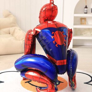 May include: A large, red and blue Spider-Man shaped balloon. The balloon is inflated and features the character's iconic design, including a red mask and suit with blue accents. The balloon is designed to stand upright.