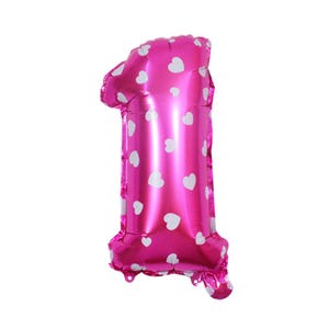 May include: A pink foil balloon in the shape of the number one. The balloon is decorated with white heart-shaped patterns. The balloon is inflated and ready for a birthday or other celebration.