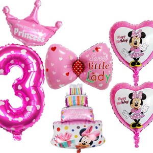 May include: Pink and white balloon decorations for a birthday party. The balloons include a number 3, a bow, a cake, a crown, and two heart-shaped balloons with Mickey Mouse characters. The balloons have the text "Happy Birthday!" and "Sweet little Lady".