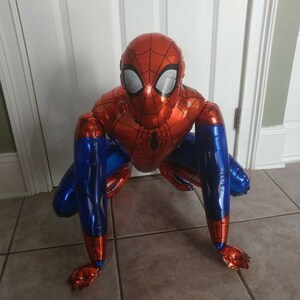 K&ouml;nnte beinhalten: Ein roter und blauer Spider-Man-Ballon in einer hockenden Pose. Der Ballon besteht aus gl&auml;nzendem, metallischem Folienmaterial.