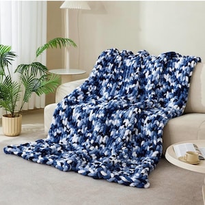 May include: A chunky knit throw blanket featuring a variegated pattern of deep navy blue, royal blue, and crisp white yarn. The blanket is constructed with thick, soft loops of chenille-style material, creating a textured, braided appearance.