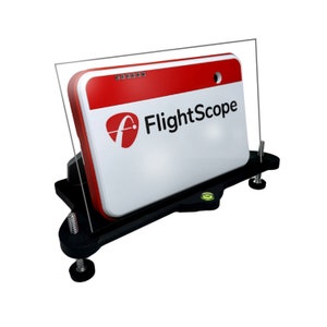 Op de afbeelding: Een zwart-witte FlightScope golf launch monitor met een rood-wit logo. De monitor is gemonteerd op een zwarte standaard met een waterpas.