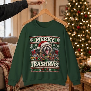 Puede incluir: Una sudadera de manga larga de color verde oscuro con un gráfico de un mapache con gorro de Papá Noel, rodeado de cubos de basura y luces navideñas. El texto dice MERRY TRASHMAS! con patrones de copos de nieve y árboles.
