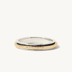 May include: A silver and gold ring with a hammered texture. The ring is made of three bands, one silver, one black, and one gold.