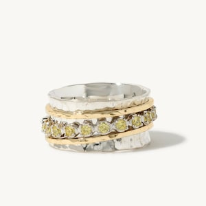 May include: A silver and gold spinning ring with a band of yellow gemstones.