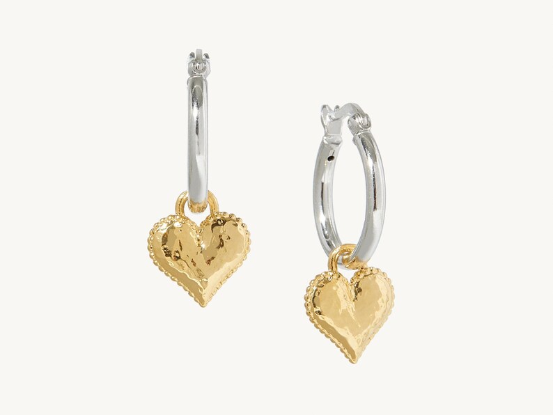 Puede incluir: Pendientes de aro de plata con un dije de coraz&oacute;n de oro. El dije de coraz&oacute;n tiene una superficie texturizada.