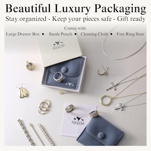 May include: A white box with a blue velvet pouch inside. The box has the text "IDEAURE" on it. The pouch has a button closure and is surrounded by various jewelry pieces, including earrings, necklaces, rings, and bracelets. The text "Comes with: Large Drawer Box, Suede Pouch, Cleaning Cloth, Free Ring Sizer" is at the top of the image.