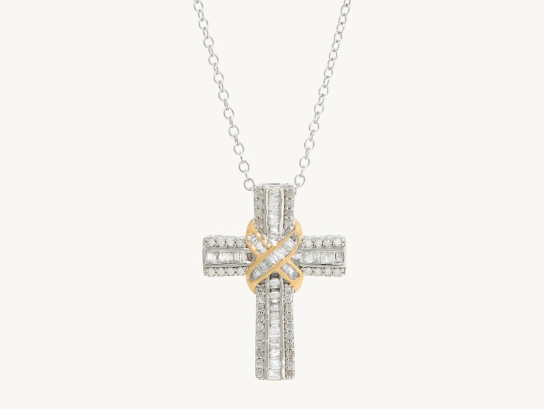 Puede incluir: Un collar de cadena de plata con un colgante de cruz engastado con diamantes. La cruz est&aacute; hecha de dos capas de diamantes, con una banda dorada en el centro.