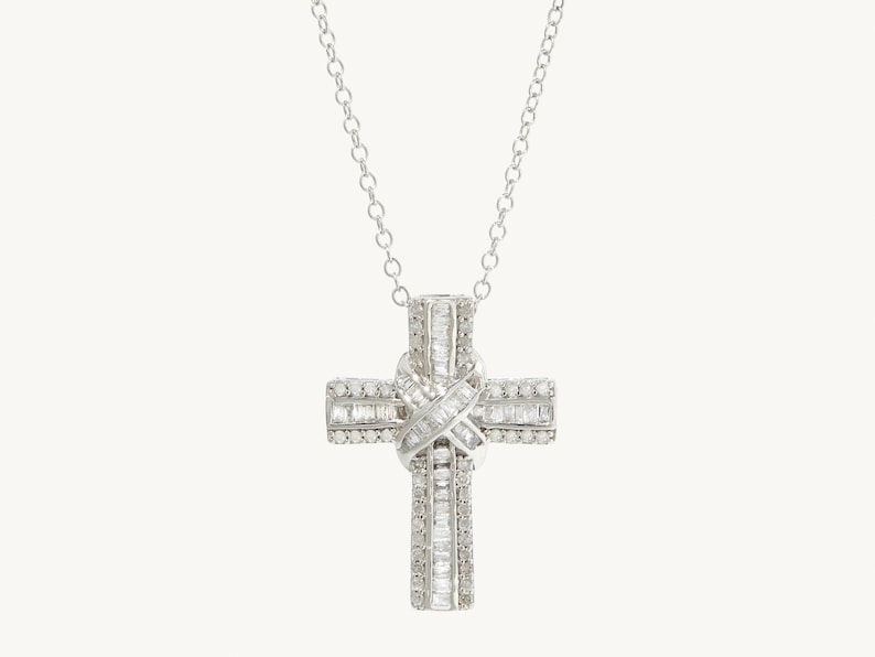 Puede incluir: Un collar de cadena de plata con un colgante de cruz engastado con diamantes. La cruz est&aacute; dise&ntilde;ada con un nudo en el centro y presenta diamantes de talla baguette.