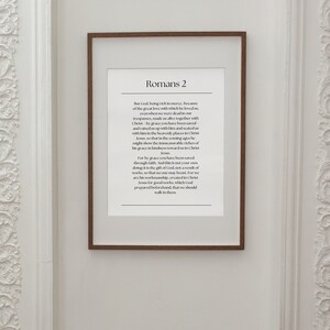 Puede incluir: Una impresión enmarcada con fondo blanco y texto negro. El texto es un versículo bíblico de Romanos 2. El marco es de madera marrón.