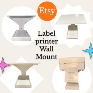 May include: White wall mount for a label printer. The mount has a shelf for the printer and a small shelf below for catching labels. The text "Etsy" and "Label printer Wall Mount" are visible in the image.