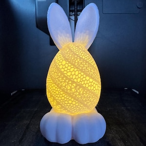 May include: A white ceramic Easter bunny night light with a lacy design. The light is on and illuminating the bunny's face.