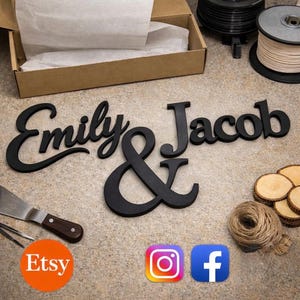 May include: Black wooden sign featuring the names "Emily & Jacob" in a decorative font. The ampersand is stylized. The Etsy, Instagram, and Facebook logos are visible in the image. The sign is displayed on a neutral surface.