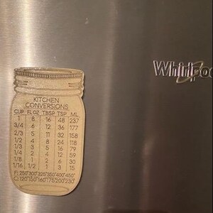 May include: A wooden kitchen conversion chart shaped like a mason jar with the text "Kitchen Conversions" and a table listing measurements in cups, fluid ounces, tablespoons, teaspoons, and milliliters.
