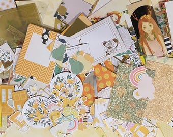 May include: A collection of yellow, green, and brown patterned paper scraps and stickers. The papers have floral, geometric, and abstract designs. The stickers feature butterflies, flowers, and other nature-inspired motifs.