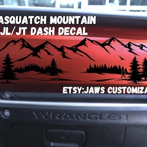 Peut inclure: Autocollant de tableau de bord Sasquatch Mountain JL/JT noir. L'autocollant présente une chaîne de montagnes, des arbres et une silhouette de Sasquatch. Le texte "Sasquatch Mountain JL/JT Dash Decal" et "Etsy: Jaws Customization" sont visibles.
