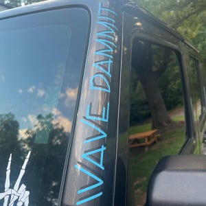 May include: A black Jeep with a blue and black "WAVE DAMN" sticker on the driver's side A-pillar.