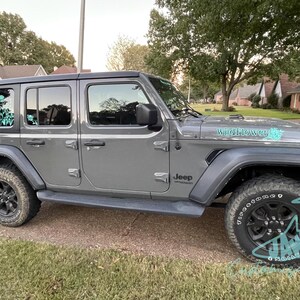 May include: A grey Jeep Wrangler with black wheels and a teal "Wildflower" decal on the bonnet. The Jeep has a teal floral design on the rear window.