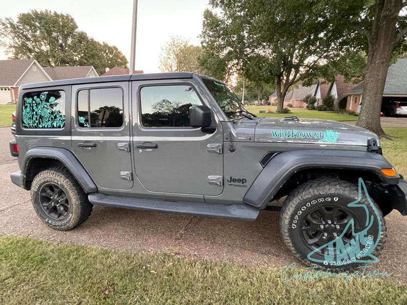 May include: A grey Jeep Wrangler with black wheels and a teal "Wildflower" decal on the bonnet. The Jeep has a teal floral design on the rear window.