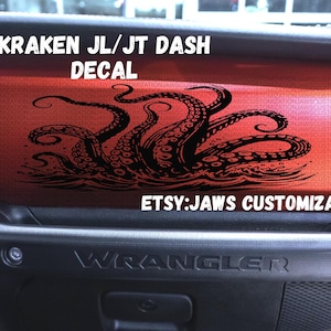 May include: A red dashboard decal with a black Kraken octopus design. The decal is for a Jeep Wrangler JL/JT model. Text on the decal reads "KRAKEN JL/JT DASH DECAL" and "ETSY:JAWS CUSTOMIZATION".
