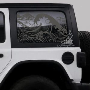 May include: A dark gray vinyl decal applied to the rear side window of a white vehicle. The decal features a detailed illustration of stylized ocean waves and a shark fin silhouette, with the text Jaws Customization printed in a script font.