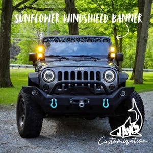 May include: A black sunflower windshield banner applied to the top of a Jeep windscreen. The banner features a repeating floral pattern. The text SUNFLOWER WINDSHIELD BANNER is written above the vehicle, and a shark logo with the text JAWS Customization is visible.