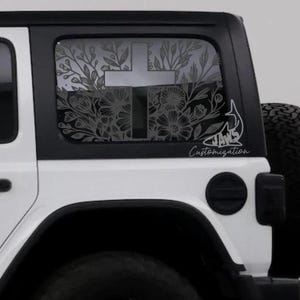 Puede incluir: Un Jeep Wrangler blanco con un diseño floral y una cruz negra en la ventana trasera. El diseño es una calcomanía de vinilo personalizada con el texto "JAWS Customization" debajo.