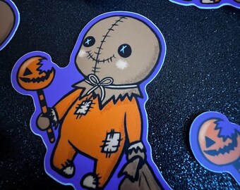 May include: A collection of Halloween-themed stickers featuring a cartoon character in an orange outfit with patches, a burlap sack head, and holding a pumpkin lollipop. The stickers have a purple outline and are on a black, glittery surface.