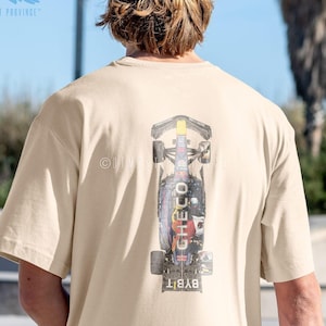 May include: Beige t-shirt with a graphic of a race car on the back. The car design includes the name "Checo" and the "Bybit" logo. The shirt has short sleeves and a relaxed fit. The brand logo "Utmost Province" is visible.