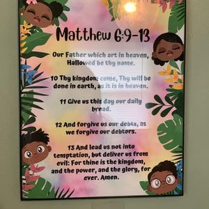 May include: A framed print featuring the text "Matthew 6:9-13" with a colorful floral and cartoon character design. The text includes a prayer. The frame is black.