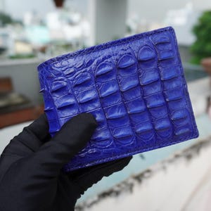 Puede incluir: Una cartera de piel de cocodrilo azul con un patrón texturizado.