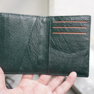 May include: Open, dark green leather wallet with a textured surface. The wallet is open, revealing several card slots and a pocket. The interior is a lighter brown color.