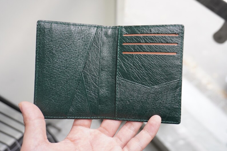 May include: Open, dark green leather wallet with a textured surface. The wallet is open, revealing several card slots and a pocket. The interior is a lighter brown color.