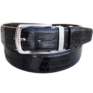 Könnte beinhalten: Ein schwarzer Gürtel aus Alligatorleder mit einer silbernen Schnalle. Die Schnalle hat eine glatte, polierte Oberfläche und ein schlichtes Design.