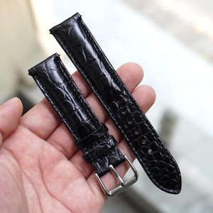 May include: Two black watch straps with a crocodile skin texture. One strap has a silver buckle. The straps are made of a shiny, durable material. The watch straps are new and ready to be attached to a watch.