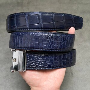 May include: Three navy blue alligator leather belts stacked on top of each other. The belts have a silver buckle.