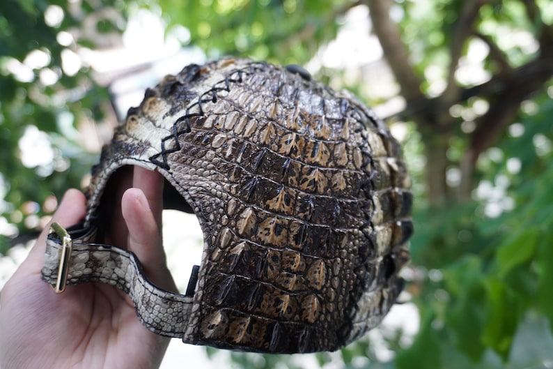 K&ouml;nnte beinhalten: Baseballcap mit einem strukturierten, braunen und beigefarbenen Krokodilhautmuster. Die Kappe hat einen gebogenen Schirm, eine goldfarbene Metallschnalle und schwarze Nahtdetails. Ein einzigartiges Accessoire.