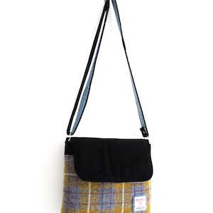 May include: A shoulder bag with a black flap and strap, and a plaid pattern in yellow, blue, and brown. The bag is hanging against a white background. The strap is black with a blue patterned lining.
