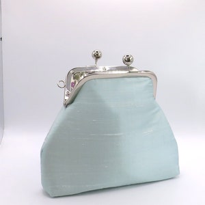 May include: A light blue coin purse with a silver clasp and two silver ball accents. The purse is made of a soft, textured fabric.