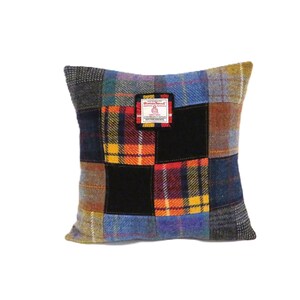 May include: Square patchwork pillow with a variety of plaid and solid fabric squares in shades of blue, yellow, red, and black. A small rectangular tag is sewn on the front. The pillow is made of a thick, textured material.
