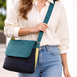 May include: A teal and navy blue messenger bag with a flap closure and adjustable strap. The bag features a teal suede-like flap and a navy blue body. The strap is teal with a yellow floral pattern on the underside.