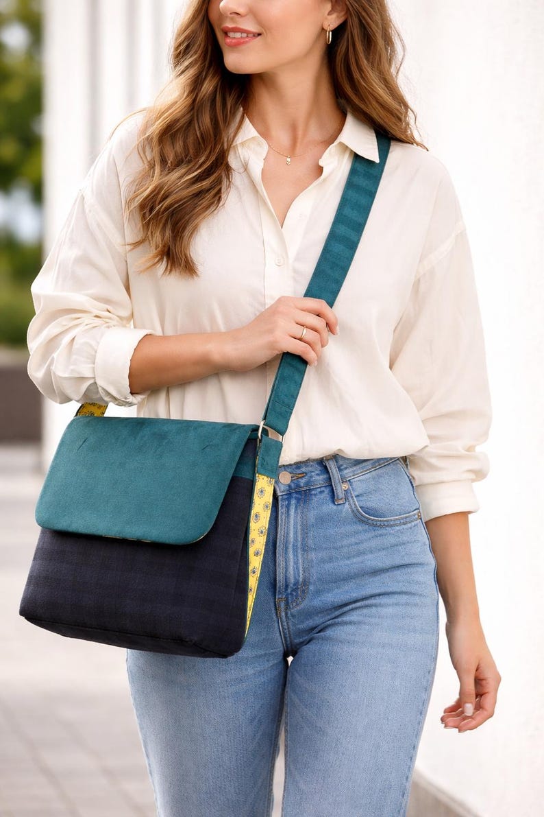 May include: A teal and navy blue messenger bag with a flap closure and adjustable strap. The bag features a teal suede-like flap and a navy blue body. The strap is teal with a yellow floral pattern on the underside.