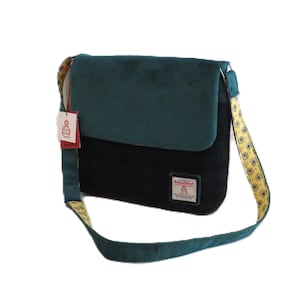 May include: A two-tone messenger bag with a teal flap and black body. The bag features a patterned strap with yellow and gold accents. A tag with the brand name is attached.