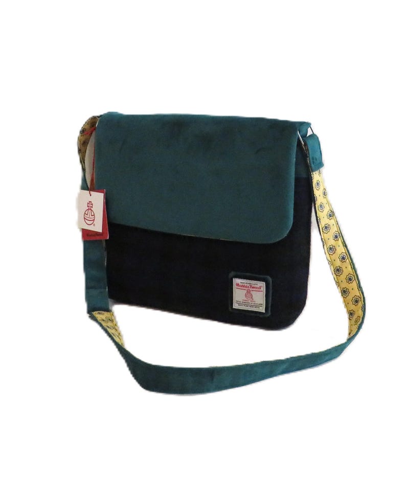 May include: A two-tone messenger bag with a teal flap and black body. The bag features a patterned strap with yellow and gold accents. A tag with the brand name is attached.